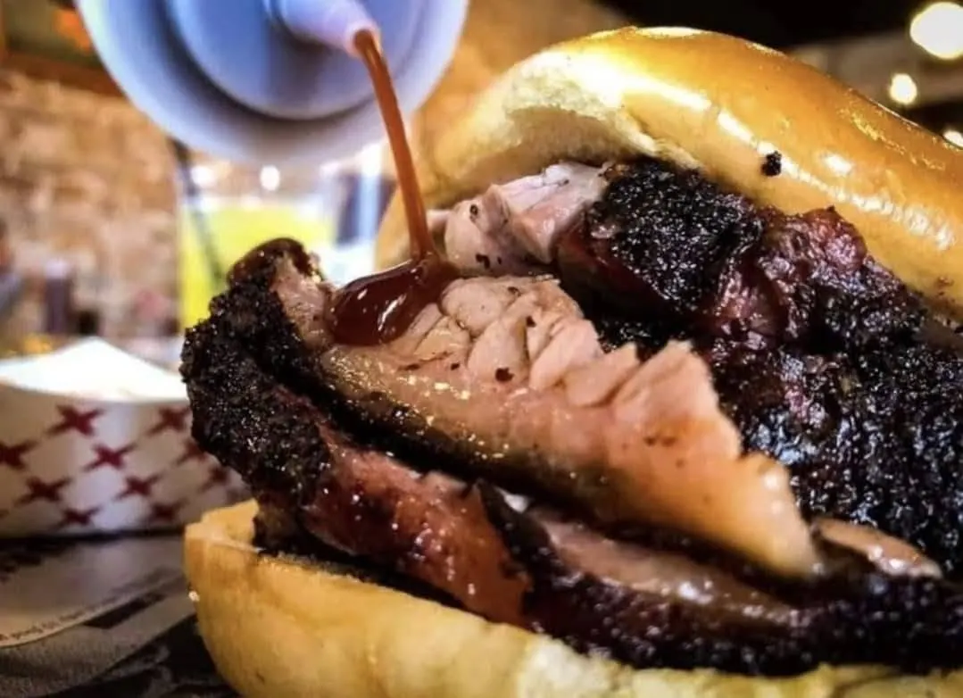 Brisket sandwich with barbecue sauce being poured over it